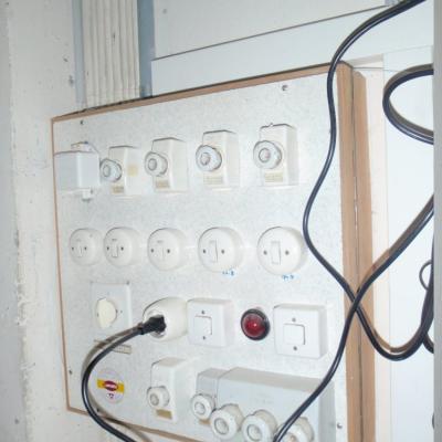 Panneau électrique en fibrociment. Sous le cadre du tableau se trouve un carton amianté (faiblement aggloméré). 